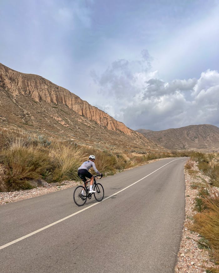 Cyclist enjoying a peaceful ride on a scenic mountain road under a cloudy sky.