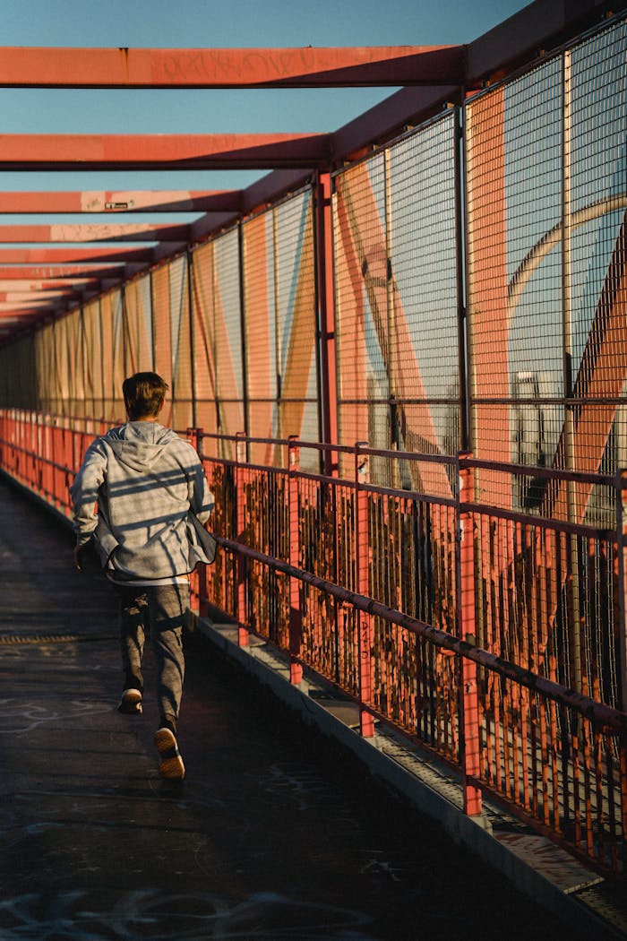 Back view of unrecognizable fit sportsman running on roofed bridge during training in city